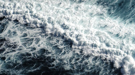 In blue water, large white waves crash violently on each other