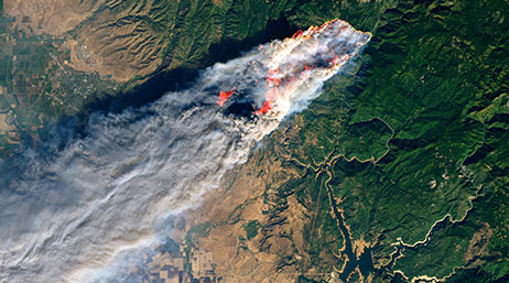 An aerial view of fire burns a large acreage of green land