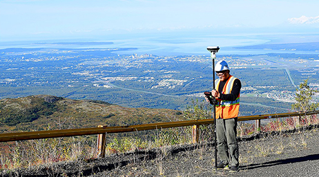 A mobile worker with equipment surveying underground electrical lines while in a high up area overlooking cities and neighborhoods
