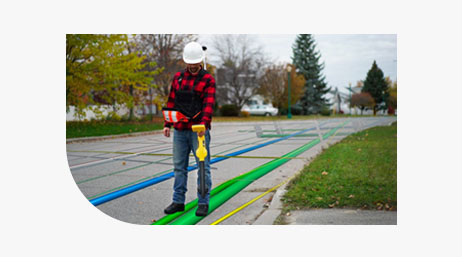 A fieldworker in a plaid shirt and a hard hat standing on a street using Eos Locate for ArcGIS to detect pipes, shown in blue and green, under the street
