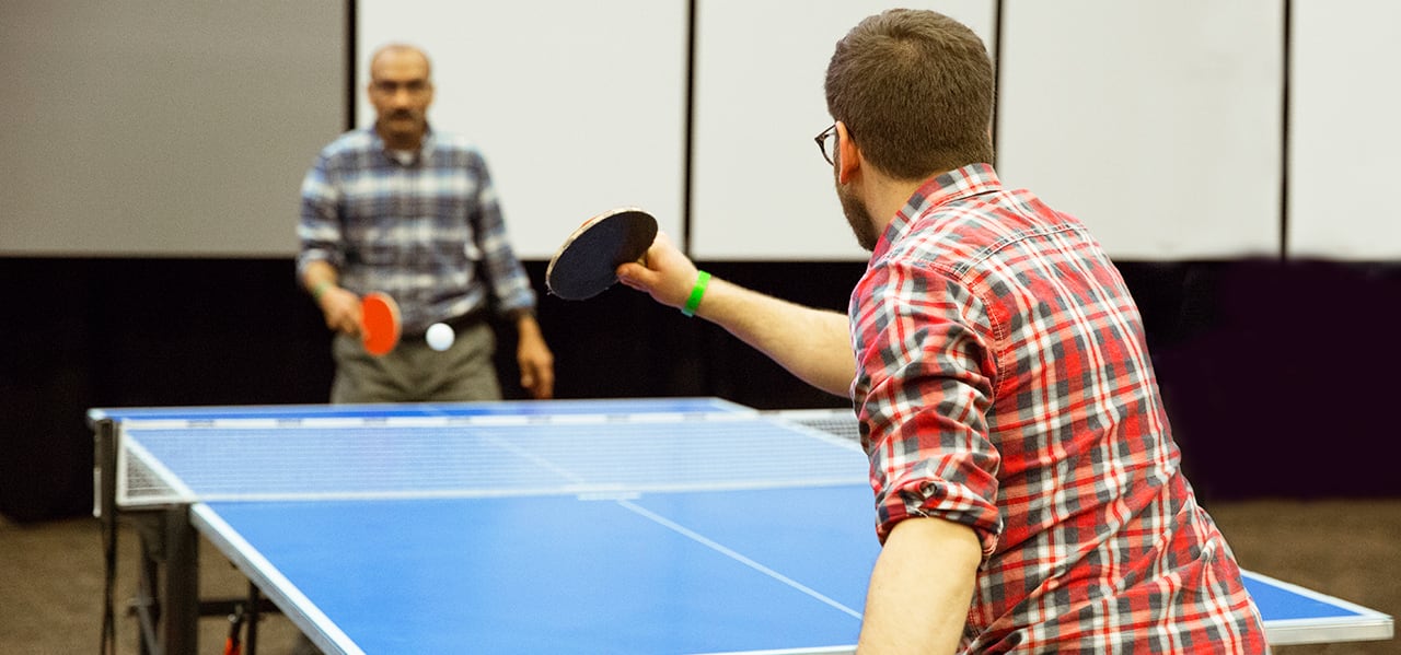 Two people in plaid shirts with sleeves rolled up playing ping pong