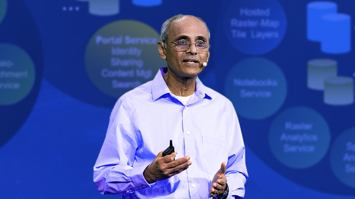 Sud Menon wearing a headset microphone speaking against a blue background with circles holding text