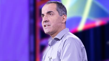 Summit presenter wearing a purple shirt looking to the right in front of a blue background with pink and yellow graphics