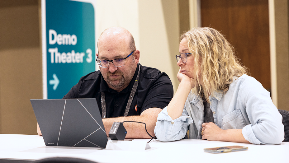 Two adults sit together at a table, focused on a laptop screen
