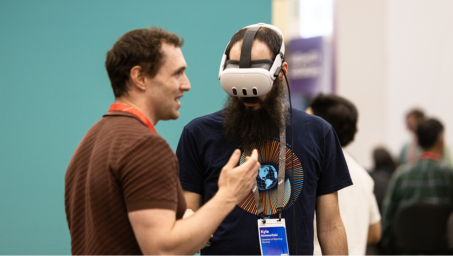 A bearded man wears a white virtual reality headset while standing indoors at a conference or tech event