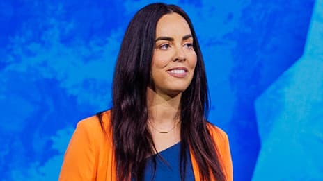 Presenter with long dark hair wearing an orange jacket and blue blouse