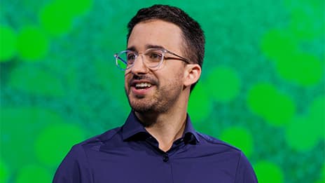 Presenter with cropped dark hair wearing glasses and a purple button up shirt