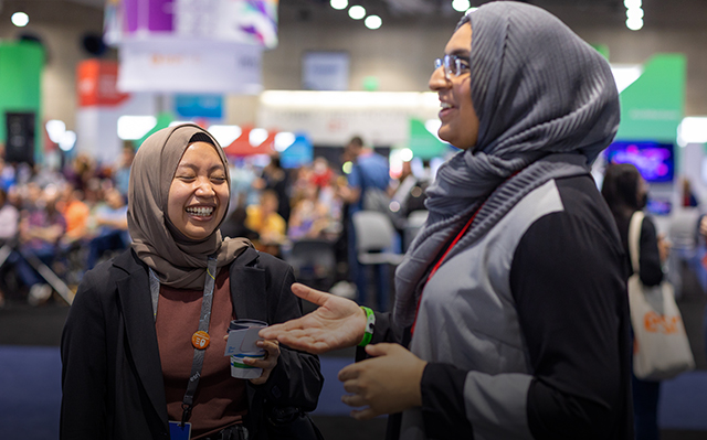 Two smiling event attendees wearing head scarves networking in the exhibition area