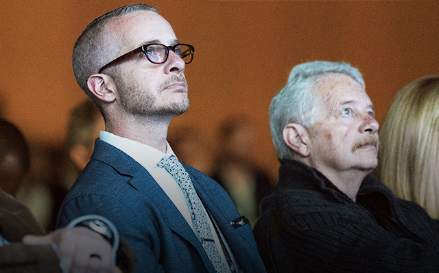 Two seated event attendees wearing collared button up shirts watching a user presentation