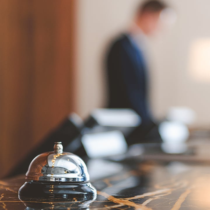 Smiling hotel desk clerk handing a hotel room key card to an unseen guest across a counter with a brass bell