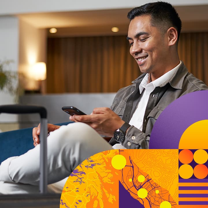 Traveler with luggage seated in a  hotel lobby, looking at a cell phone