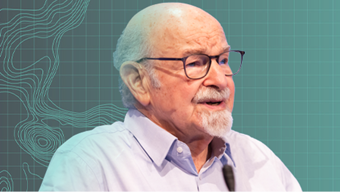 Portrait of a speaker with a gray goatee wearing glasses against a blue-green gradient background with a grid and contour map lines