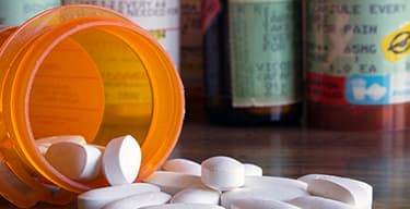 Close-up of white oval pills spilling from orange plastic prescription bottle with more prescription bottles in background