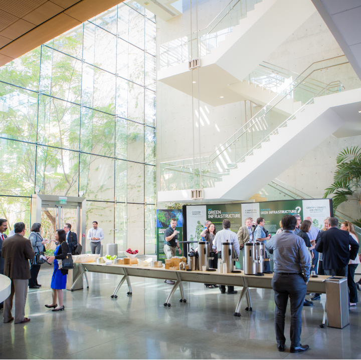 Conference attendees in a large atrium with a glass wall, a staircase, a buffet table, and a display about green infrastructure