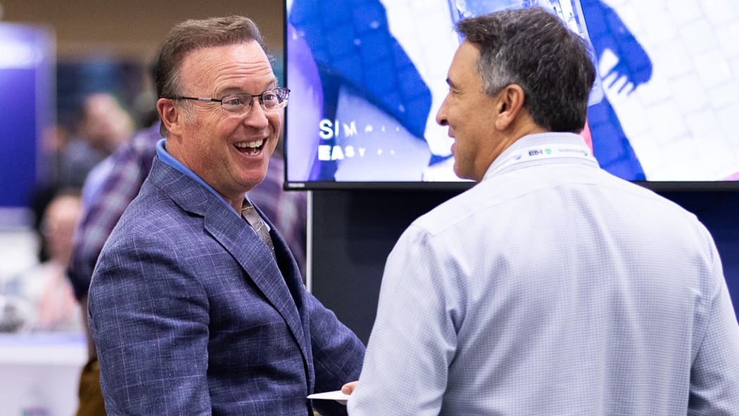 Two people interacting at a booth in the Expo; one is smiling broadly