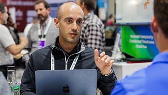 GIS expert with a laptop gestures while speaking with a conference attendee, whose face we cannot see