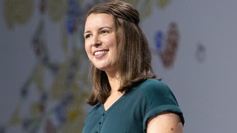 Presenter with shoulder length brown hair wearing a teal blouse and smiling