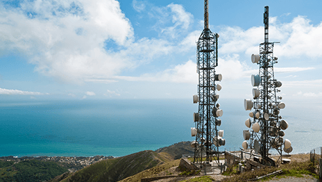 Two cellular communications towers on a hill overlooking a body of water
