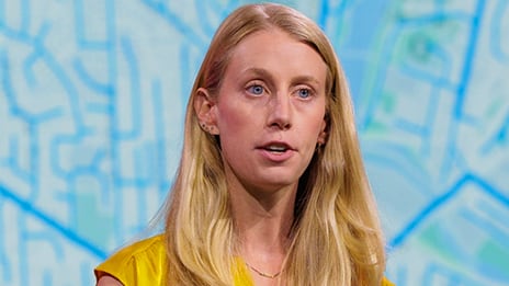 Presenter with long blonde hair agains a blue map background