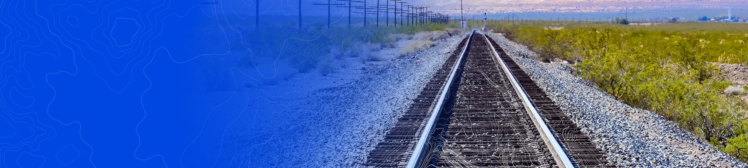 Train tracks overlaid with faint map elements receding into the distance with a gravel bed and grass on the right
