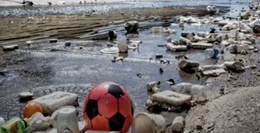Waterway with a soccer ball, beverage can, and other debris along the shoreline