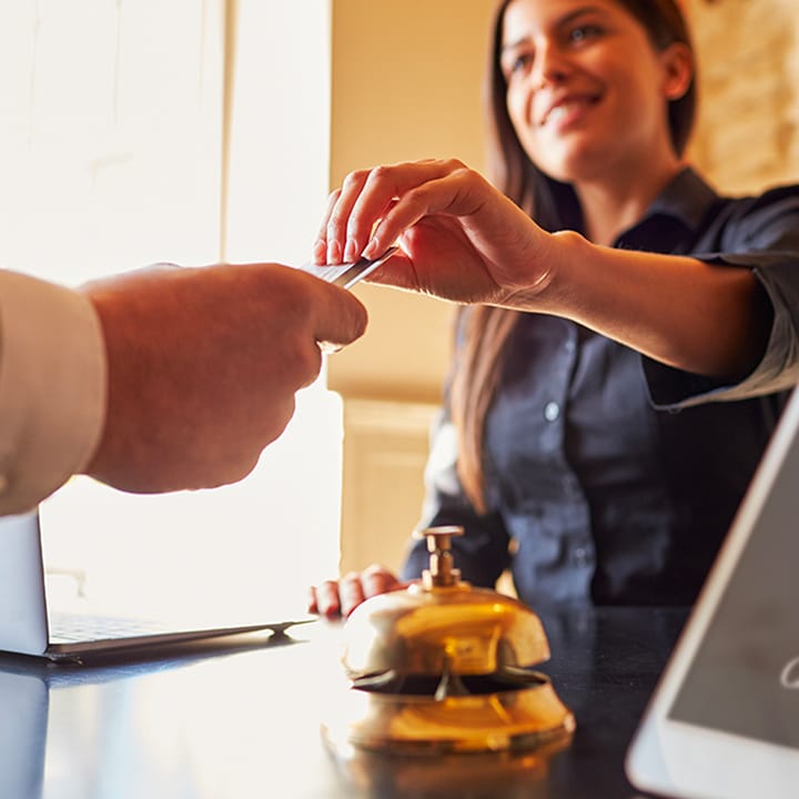 Extended hand of a guest giving a credit card to a smiling hotel employee working behind the front desk.