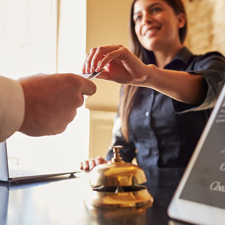 A hotel employee working at the front desk smiling and accepting a credit card from a guest with their hand outstretched
