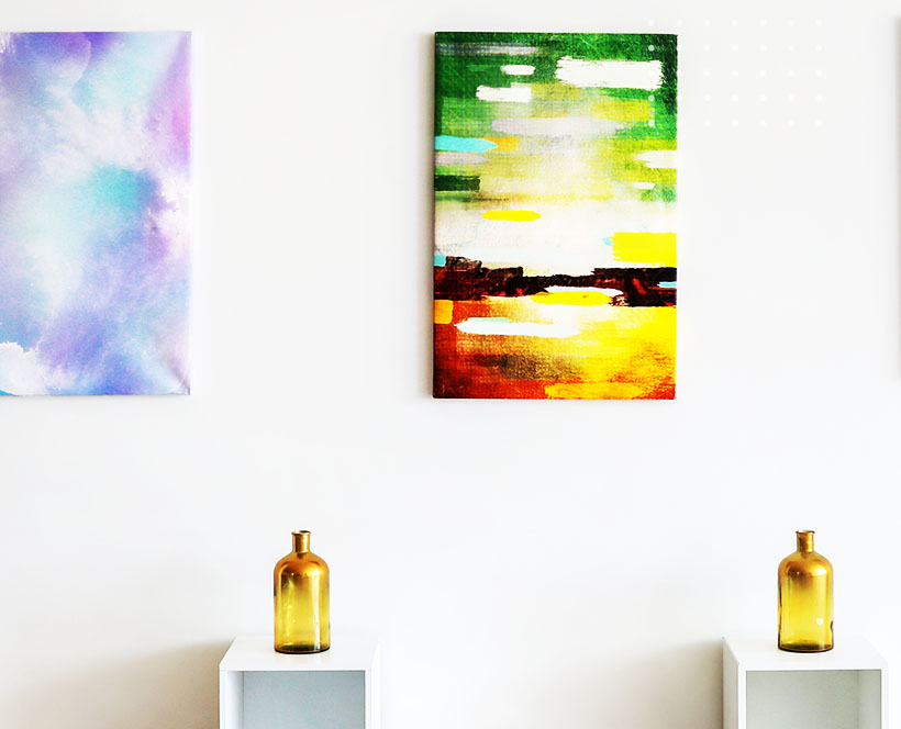 An art gallery wall with two hanging canvases and a glass bottle on display