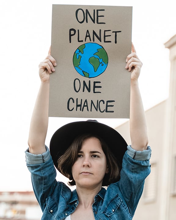 A person holds up a sign that reads "One planet, one chance” with a drawing of Earth