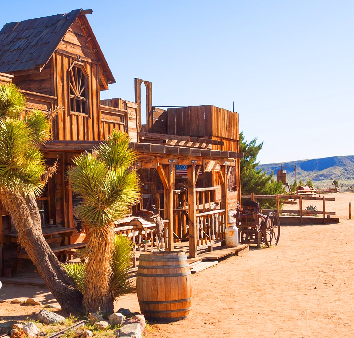 Historic wooden storefronts in Frontier Town, Montana, with a barrel-lined boardwalk and yucca plants