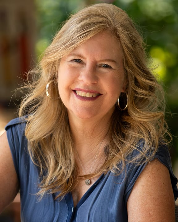 Susan Straight smiling wearing hoop earrings and a blue blouse