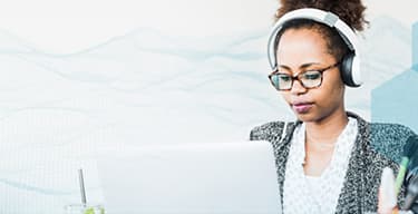Woman with glasses and wearing white headphones uses a laptop