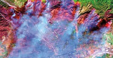 looking down through blue clouds at a colorful topographic map in green, blue, brown, pink and purple