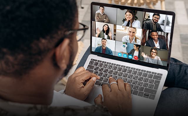 A person sitting down holds thon a computer during a virtual conference meeting with colleagues