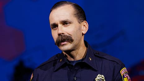 Closeup portrait of a presenter from CAL FIRE with a mustache against a blue stage backdrop