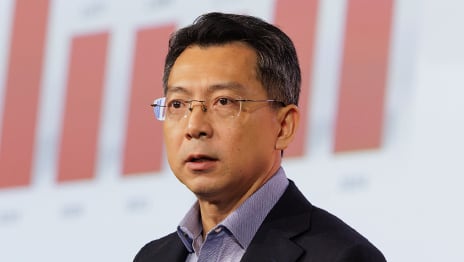 Serious speaker with short dark hair and rimless glasses looking to the left