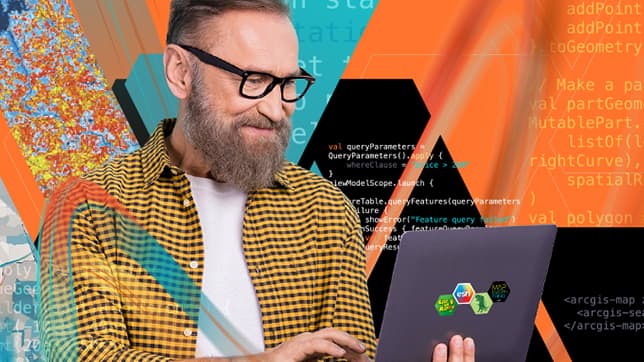 A person wearing glasses and a yellow and black checkered shirt is smiling while holding a laptop in front of abstract coding and map graphics
