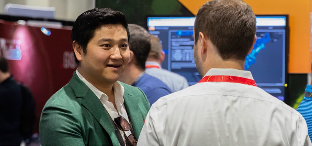 Attendee wearing a green sports coat smiling as they talk with an Esri expert wearing a red lanyard