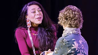 Attendee wearing a magenta blouse and colorful tribal beaded earrings warmly shaking the hand of another attendee wearing a floral top