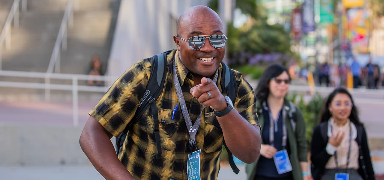 Happy attendee wearing mirrored aviator glasses and a black and yellow plaid button up shirt points playfully at the camera during an event