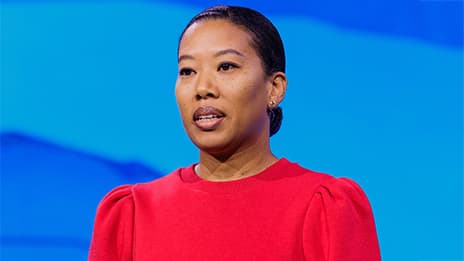 Presenter wearing bright red looks slightly to the left while onstage