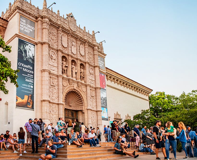 Exterior of the San Diego Museum of Art featuring an ornate facade and arched entrance with a crowd gathered on the steps