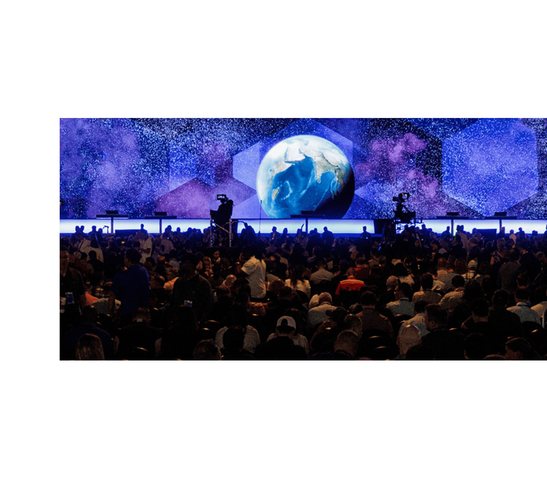Darkened room with a large audience facing a stage with a glowing Earth on a digital backdrop