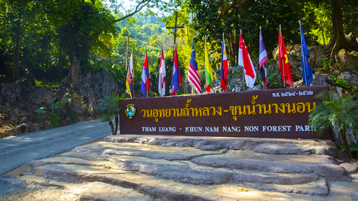 Sign at the entrance to the Tham Luang cave with the flags of countries above it who assisted in the rescue 