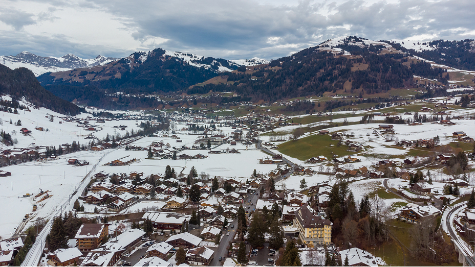 An aerial view of a rural town dusted with snow with mountains rising in the background 