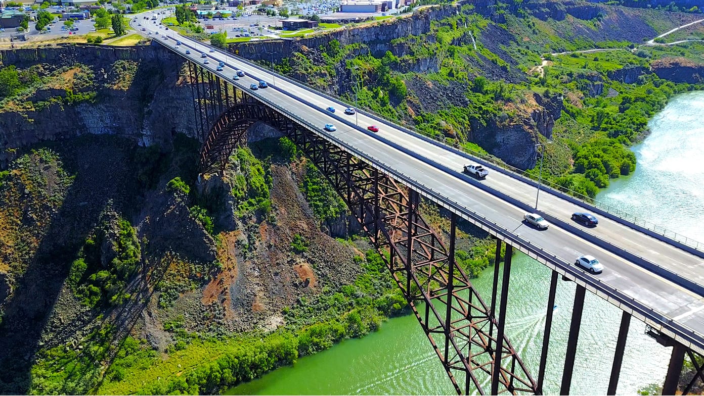 Aerial image of cars on a four-lane bridge high above a rippling green river 