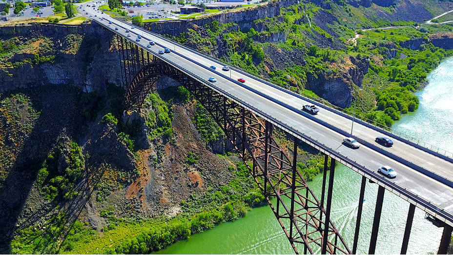 Cars crossing a tall bridge over a river on a sunny day