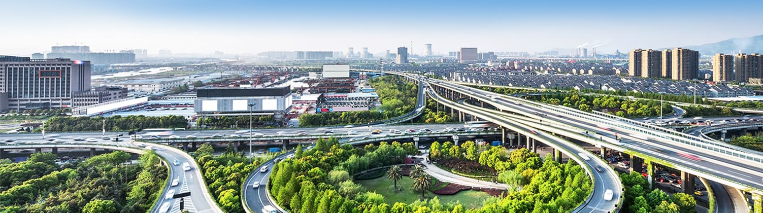 A city with skyrises, houses, a stadium, and trees surrounding the interstate and intersecting overpass that runs through the middle of the city
