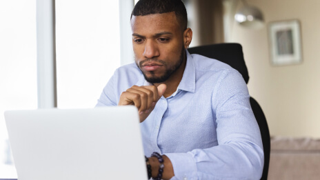  在一间灯火通明的现代化办公室内，一个身着浅蓝色有领衬衫的人正聚精会神地注视着一台笔记本电脑的显示屏