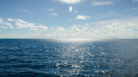A view of the ocean with the sun reflecting on it with clouds overhead